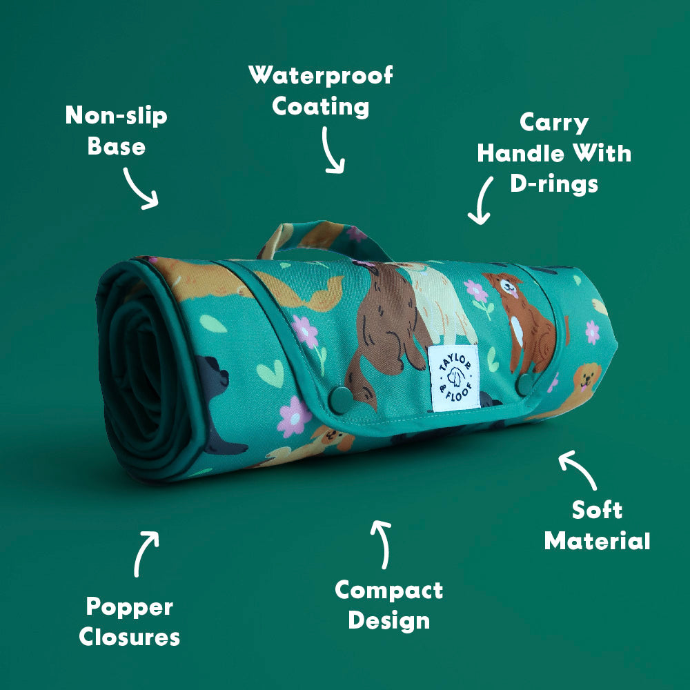 Roll-up dog mat with dog illustrations on a green background, featuring text labels about its features. Features including, non slip base, waterproof coating, carry handle with d rings, soft material, compact design and popper closures.