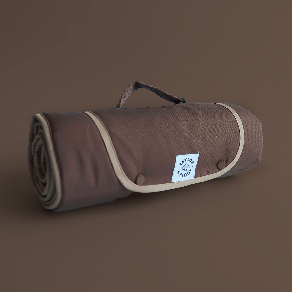 Roll-up brown mat with beige border and handle on a brown background