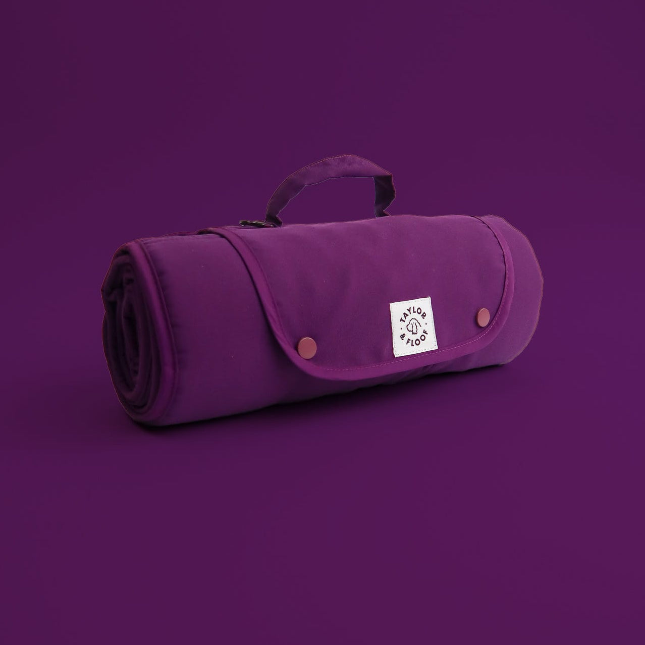 Purple rolled-up travel mat for dogs with a Taylor and Floof logo on a purple background