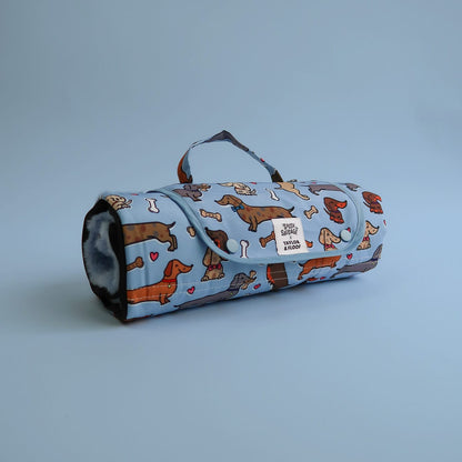 Waterproof dog settle mat in a lovely dachshund resign. Rolled up for potable use on a blue background.
