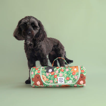 Dog standing next to a cockapoo illustrated floral settle mat. Rolled up and on a light green background colour.