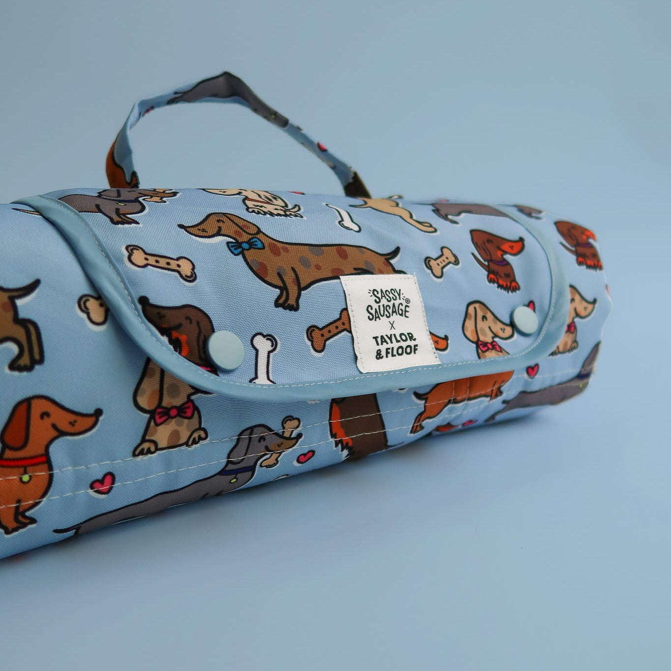 Dog settle mat folded with popper closure and D ring attachment. Waterproof dog settle mat with cute sausage dog design. 