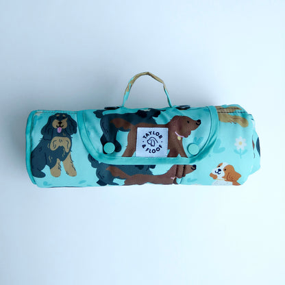 Roll-up blanket with spaniel pattern and visible brand logo on a light gray background. Light blue waterproof dog settle mat featuring cute spaniel illustrations perfect for cocker, springer, and cavalier spaniel lovers.
