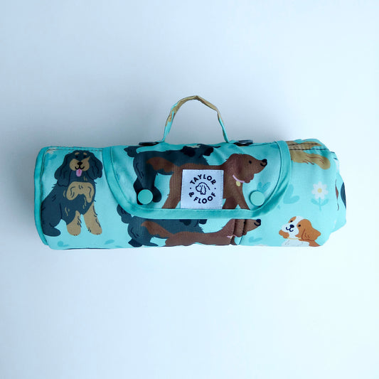 Roll-up blanket with spaniel pattern and visible brand logo on a light gray background. Light blue waterproof dog settle mat featuring cute spaniel illustrations perfect for cocker, springer, and cavalier spaniel lovers.