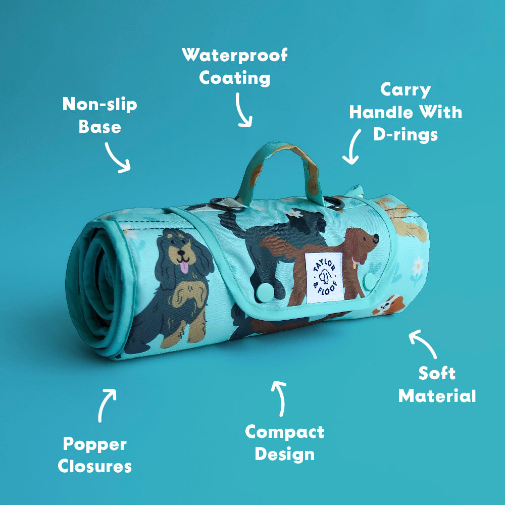Roll-up mat with Spaniel illustrations on a blue background, featuring text labels about its features. Features including waterproof coating on material, non-slip base, carry handle with D-rings, popper closures, compact design and soft material.