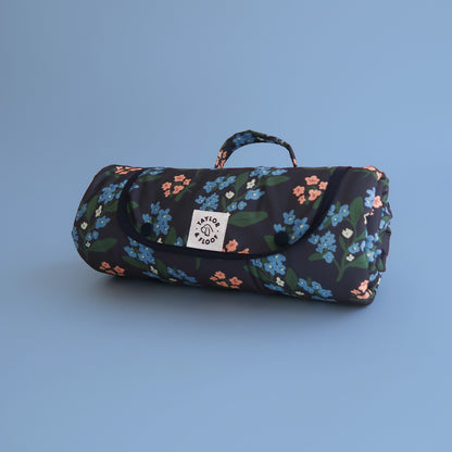 Portable dog travel mat rolled up. In Dark blue design with pink and blue florals on. 